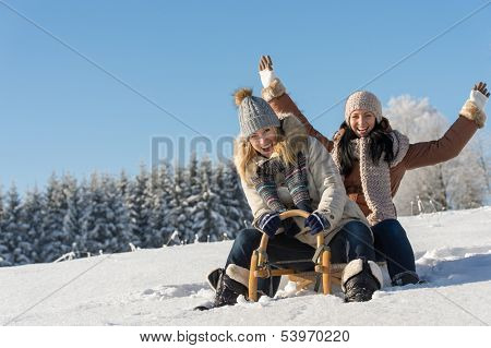 Two girlfriends sledge downhill in sunny wintertime snow wooden sledge