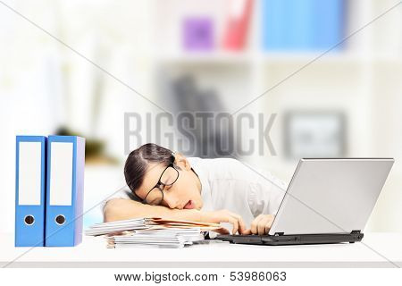 Exhausted young businessman sleeping on a desk in his office