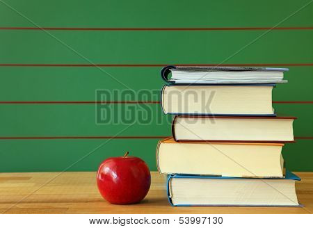 Stack of book and red apple on desk.