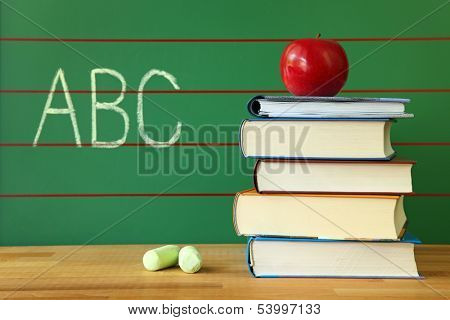 Stack of book and red apple on desk with abc written on the chalkboard