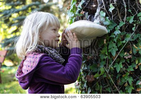 Little caucasian girl examining large Tinder fungus on tree bark - early education 