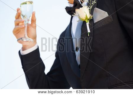 Close-up mid section of beautiful flowers on lapel of male as he holds champagne glass