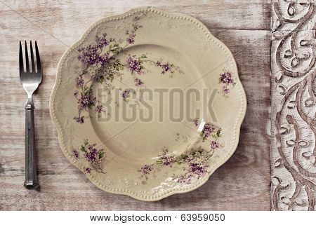 Antique decorative dinner plate (with authentic surface crazing) and vintage pewter fork on distressed wood with decorative carved border. 