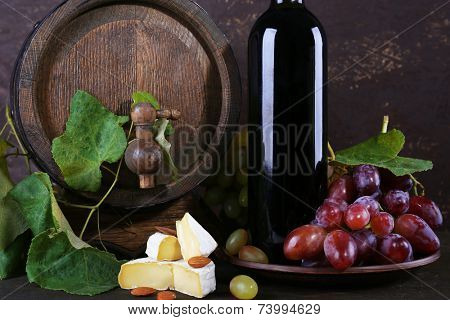 Wine in bottle and in goblet, Camembert cheese, grapes and wooden barrel on wooden table on wooden background