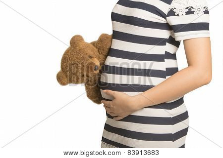 Close Up On Pregnant Belly. Woman Expecting A Baby With A Cute Teddy Bear Peaking At Her Belly.