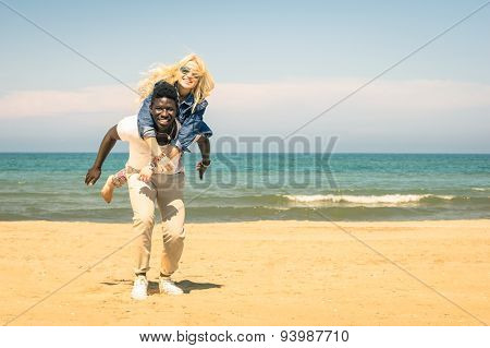 Young Multiracial Couple At The Beach Having Fun With Piggyback Jump - Happy Mixed Race Relationship