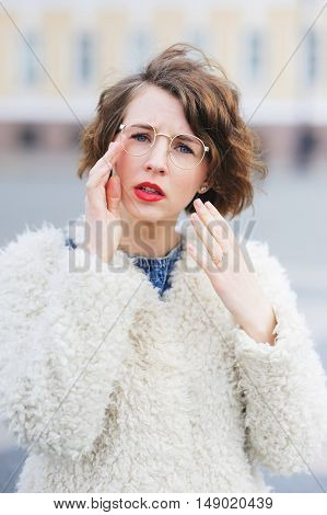 Young Beautiful Girl Student In A White Jacket In The Town Square With Narrowed Eyes Looking Through