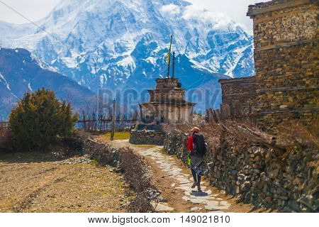 Young Pretty Woman Wearing Red Jacket Backpack Trail Mountains.Mountain Trekking Rocks Path Village. Snow Landscape View Background. Horizontal Photo