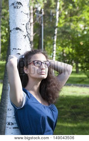 The girl looks up while standing next to a birch