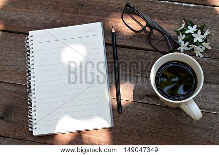 Good morning or working concept : Cup of coffee, glasses, notebook paper, pencil and white flowers on wood background