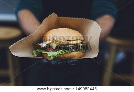 Fresh burger cooked at barbecue outdoors in craft paper. Cookout american bbq food. Big hamburger with steak meat and vegetables closeup with chef unfocused at background. Street food, fast food.