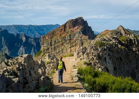 Woman hiker with green backpack doing her hike of Pico Arieiro to Pico Ruivo hiking route. Madeira island, Portugal.