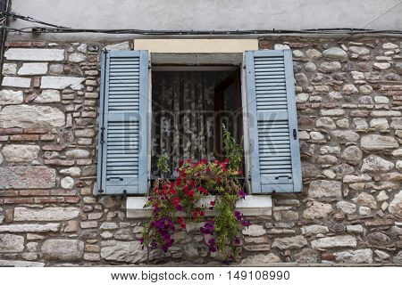 Old window with open shutters with flowers on the window sill on the stone wall. Italian Village.