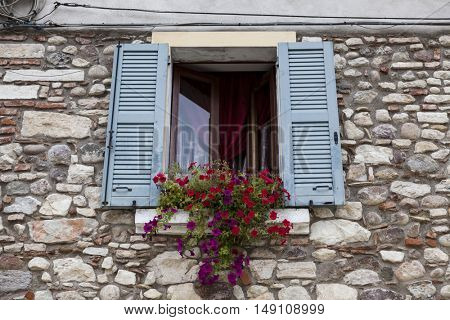 Old window with open shutters with flowers on the window sill on the stone wall. Italian Village.