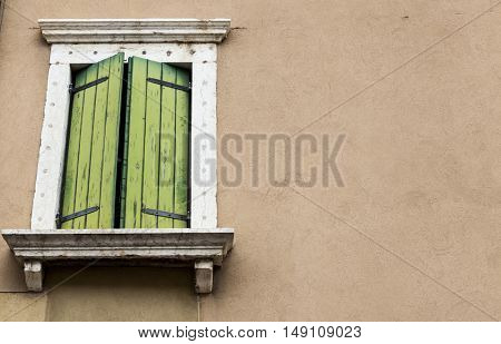 Old window with closed shutters with flowers on the window sill on the stone wall. Italian Village.