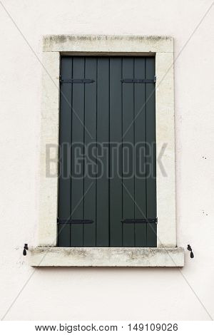 Old window with closed shutters with flowers on the window sill on the stone wall. Italian Village.