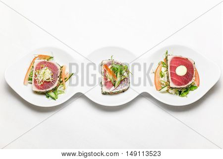sushi serving-three pieces of Tuna with chpped vegetables on a white plate, horizontal