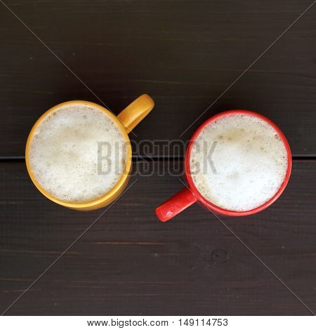 frothy cappuccino in the colored mugs on the dark wooden surface top view / coffee with whipped milk