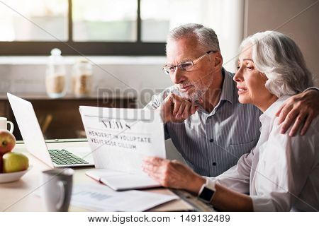 Family life. Retired husband and wife hugging each other at the dinner table while sharing the news from the media