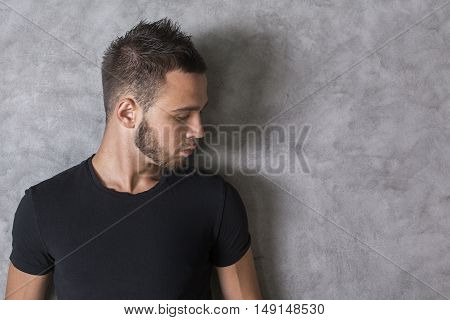 Side view of handsome caucasian guy in black T-shirt on textured concrete wall background
