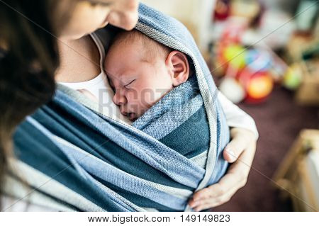 Close up of unrecognizable young mother with her newborn baby son in sling at home