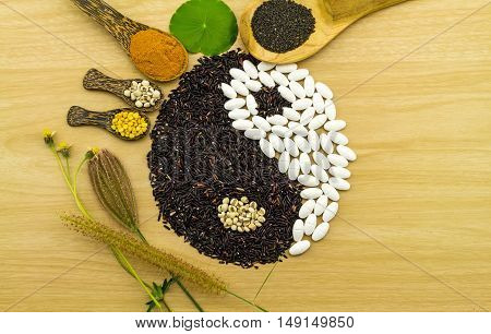 Black rice and white pill forming a yin yang symbol and  turmeric powder , millet , soybean , basil seed in wooden spoon on brown wooden blending of herb and medicine
