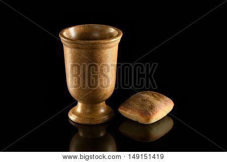 Cup of wine and bread on reflective table over dark background