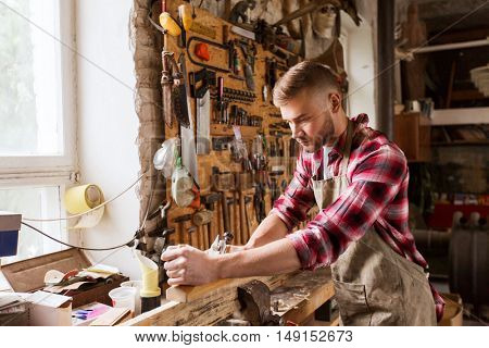 profession, carpentry, woodwork and people concept - carpenter working with plane and wood plank at workshop