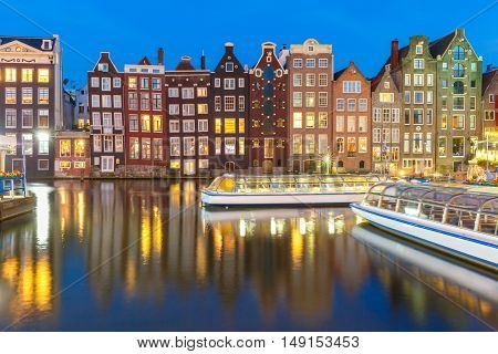 Beautiful typical Dutch dancing houses and tourist boats at the Amsterdam canal Damrak at night, Holland, Netherlands.