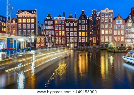 Beautiful typical Dutch dancing houses and tourist boats at the Amsterdam canal Damrak at night, Holland, Netherlands.