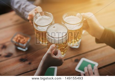 people, leisure and drinks concept - close up of hands clinking beer mugs at bar or pub