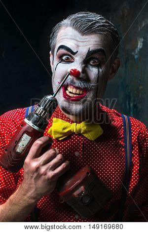 The scary clown and electric drill on dack. Halloween concept of horror and murderer