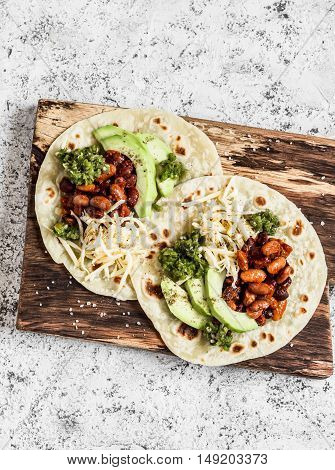 Spicy beans avocado and green chile sauce tortilla on a rustic cutting board on a light background. Top view