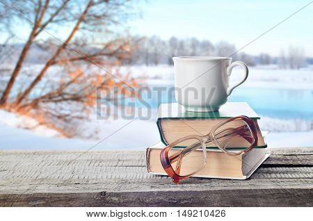 Coffee, tea or hot cocoa chocolate cup on books with eyeglasses outdoors in winter. Pile of books, glasses and white coffee cup in nature.