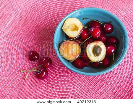 fresh cherries and apricot in green bowl on a pink wicker place mat. Refreshing background