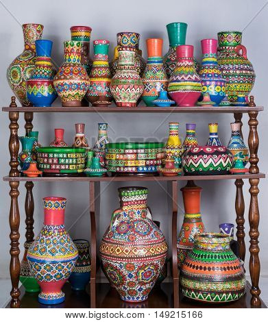 Group of colorful painted pottery vases stacked in wooden storage shelves over white wall