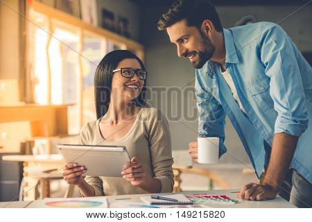 Beautiful couple of designers in casual clothes is using a digital tablet talking and smiling while working in studio