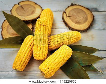 fresh corn with leaves yellow  on a white wooden table with green leaves