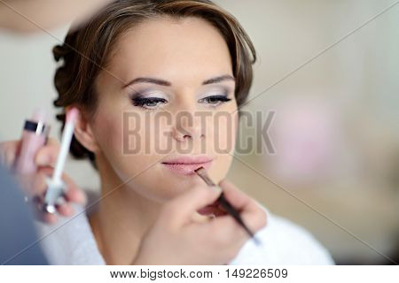 Wedding makeup artist making a make up for bride. Beautiful sexy model girl indoors. Beauty woman with curly hair. Female portrait. Bridal morning of a cute lady. Close-up hands near face