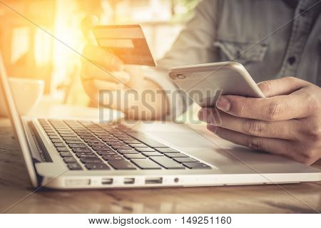 Online paymentMan's hands holding smartphone and using credit card for online shopping with vintage filter effect