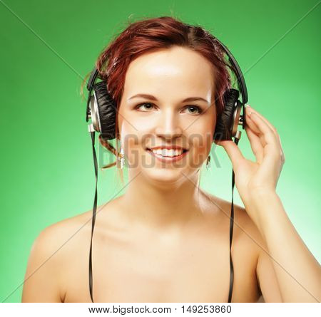Young happy woman listening to music with headhones over green background