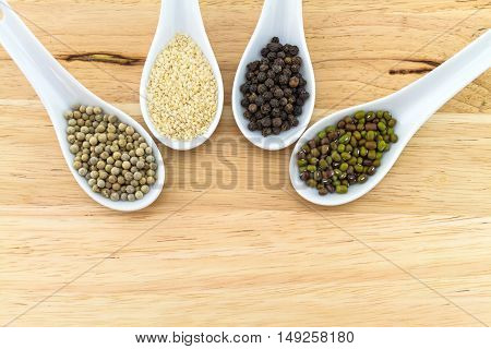 Green bean white sesame black and white pepper in white ceramic spoon on block wooden background