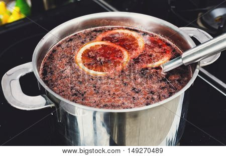 Making mulled wine for sale at country fair. Glintwine with citrus and cloves in big metal stock pot, mixed with soup ladle.