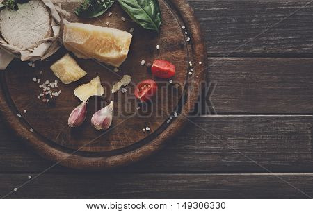 Cheese delikatessen closeup on rustic wood. Wooden desk with parmesan, camembert and brie cuts decorated with garlic, tomato and basil, top view image with copy space, soft toning