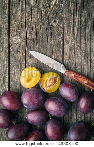 Halved ripe plums and knife on old wooden table. Top view.