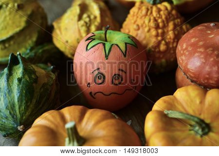 an apple disguised as a pumpkin with a funny face trying to go unnoticed between different real pumpkins