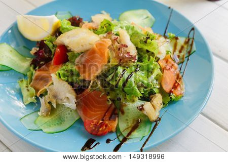 Restaurant healthy food, seafood salad closeup. Salmon and cod fish salad with vegetables and lettuce on blue plate. Appetizing dish served with sauce, dinner meal. Selective focus