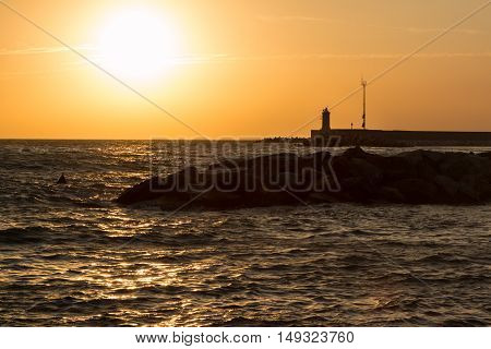 Silhouette Of Lighthouse, Reef, And Choppy Sea At Sunset
