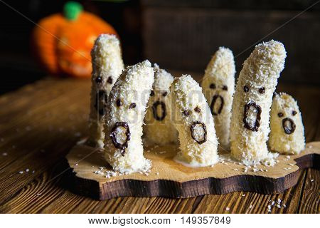 Homemade halloween scary banana ghosts monsters with chocolate faces. funny dessert recipe for party decoration fruits on vintage wooden table background
