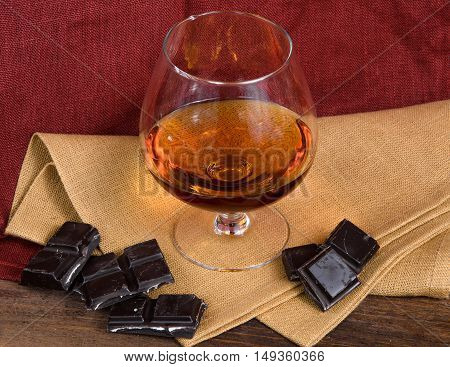Glass of brandy and a chocolate on a old wooden table